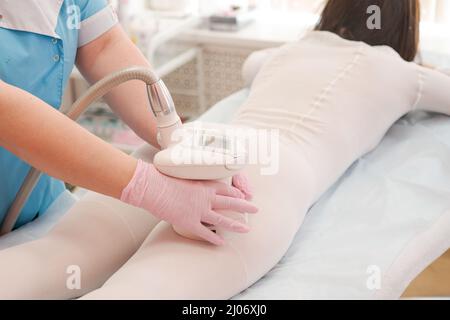 Primo piano giovane donna in abito bianco sottoposto a massaggio cosmetico di tipo liquido e lipolisi laser. Procedura cosmetica, in un centro medico. Procedure anticellulite. Foto Stock