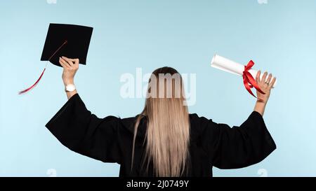 Ragazza laureata in cerimonia di laurea con certificato di diploma legato con nastro rosso e cappuccio di laurea. Donna che festeggia la laurea, vista posteriore. Istruzione in liceo, università, college Foto Stock