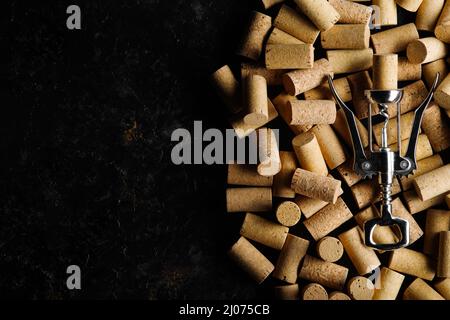 Cavatappi in metallo per aprire i tappi di vino sullo sfondo dei tappi di vino. Su sfondo nero con spazio per testo, vista dall'alto. Concetto di vendita di vino e pubblicità Foto Stock