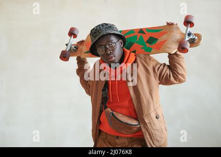 Ritratto orizzontale medio studio di bel ragazzo afroamericano vestito casual in posa su fotocamera con skateboard, spazio copia Foto Stock