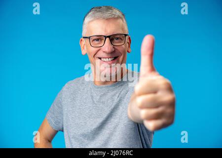 Felice positivo bel vecchio uomo mostra OK segno su sfondo blu Foto Stock