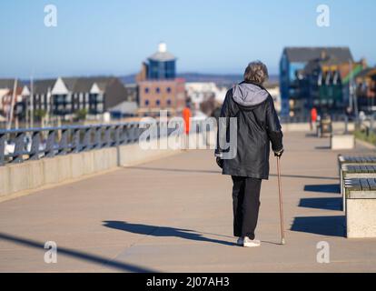 Donna anziana che cammina con un bastone per camminare / aiuto per camminare lungo un alzaia lungo il fiume nel Regno Unito. Foto Stock