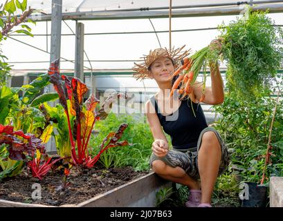Donna felice con mazzo di carote appena raccolte nel giardino sul cortile. Agricoltura biologica, cibo sano stile di vita da fattoria a tavola. Foto Stock