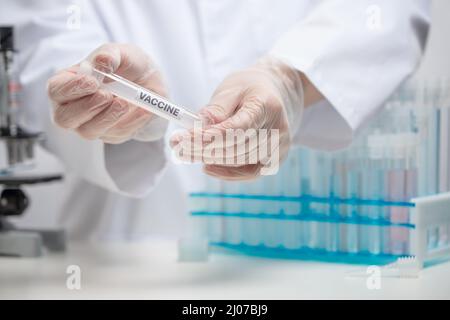 Microbiologo in guanti protettivi con provetta biologica di vaccino covid-19 su sfondo di laboratorio. Backstage della scoperta scientifica. Assistenza sanitaria a Foto Stock