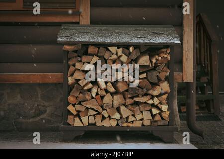 Legna da ardere. Mucchio di legna da ardere vicino a una casa di legno in una giornata invernale nevosa. Legna da ardere vicino a una casa di legno Foto Stock