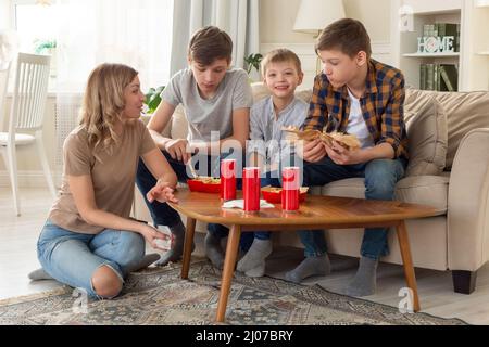 Una famiglia felice, una donna e tre ragazzi adolescenti, mangiando fast food in scatole rosse e bevendo bevande in lattine rosse. Foto Stock