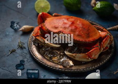 Granchio re cotto con cubetti di ghiaccio servito con lime e conchiglie su sfondo di marmo blu scuro. Concetto di pesce. Delizioso pasto sano. Libro di cucina illu Foto Stock