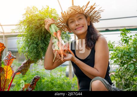 Donna felice con mazzo di carote appena raccolte nel giardino sul cortile. Agricoltura biologica, cibo sano stile di vita da fattoria a tavola. Foto Stock