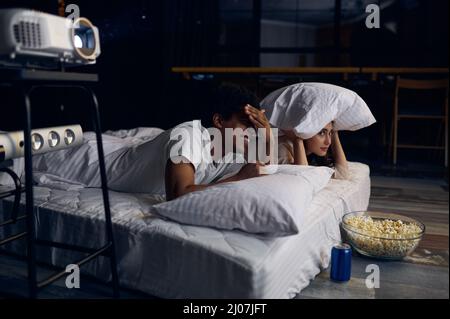 Divertente coppia che guarda film horror in camera da letto Foto Stock