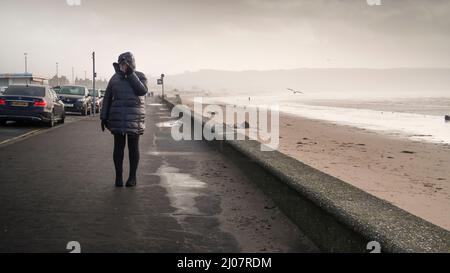 Donna che cammina con il vento a corda sul lungomare di Ayr Foto Stock