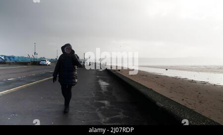 Donna che cammina con il vento a corda sul lungomare di Ayr Foto Stock