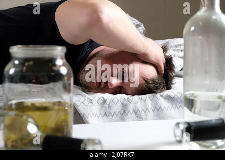 Un uomo ubriaco si trova a letto, tenendogli le mani in testa. Hangover, delirio alcolico. Foto Stock