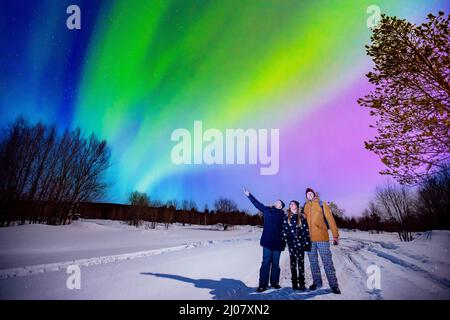 Compagnia di amici turisti guarda aurora luci nord notte a foresta, fuoco morbido. Foto Stock