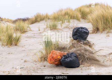 Sacchetti di plastica neri e arancioni pieni di rifiuti raccolti durante una pulizia presso la spiaggia nei Paesi Bassi. Foto Stock