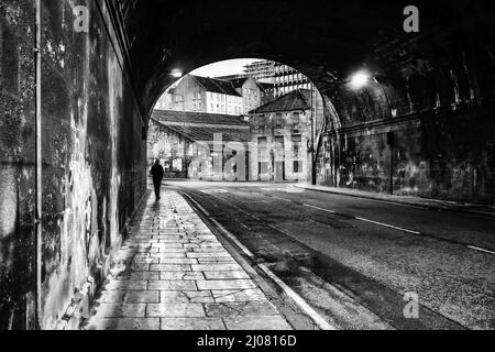 Persona che cammina attraverso un tunnel in un monotone B&W Moody, preso a King's Bridge, la stalla strada dei re passa sotto Edimburgo il 27th marzo 2017 Foto Stock