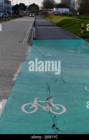 Percorso ciclabile a colori con logo bici con crepe e danni alla superficie dove il percorso attraversa il bivio stradale. Foto Stock