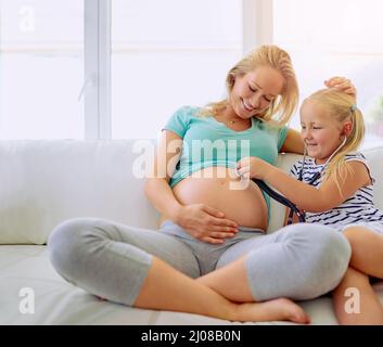 Sembra che il bambino voglia uscire ora. Scatto di una bambina usando uno stetoscopio per ascoltare le sue madri ventre incinta a casa. Foto Stock