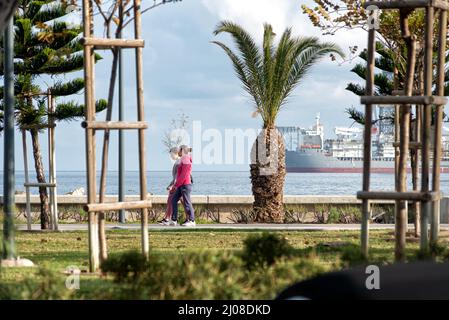 Limassol, Cipro - 22 febbraio 2019: Persone a piedi al parco di Molos Seaside con perforazione offshore sullo sfondo Foto Stock