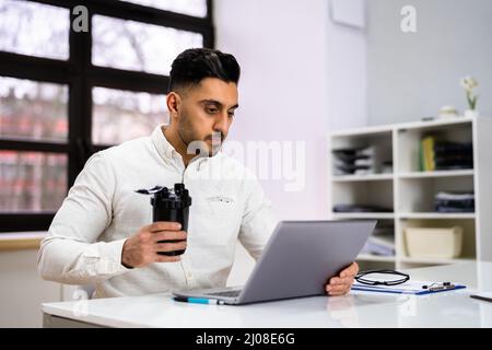 Protein Shake su scrivania e uomo in primo piano utilizzando il computer Foto Stock