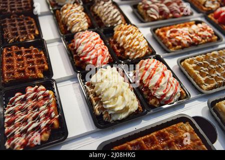 Vari tipi di cialde belghe tradizionali conditi con cioccolato, speculoos, panna montata e frutta in un negozio a Bruxelles Foto Stock