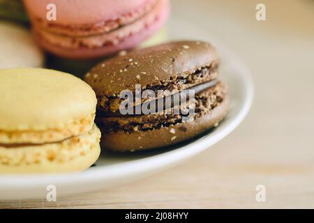 Primo piano di macaron di cioccolato, limone e lampone su un semplice piatto bianco Foto Stock