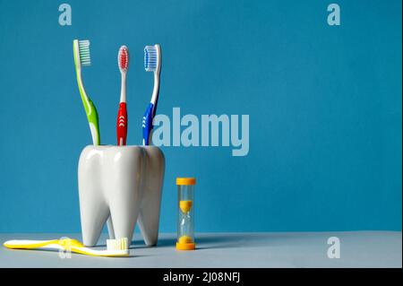 Gli spazzolini multicolore sono in vetro, a forma di dente, sul tavolo c'è un pennello di colore molto colorato e giallo clessidra per contare il ti Foto Stock