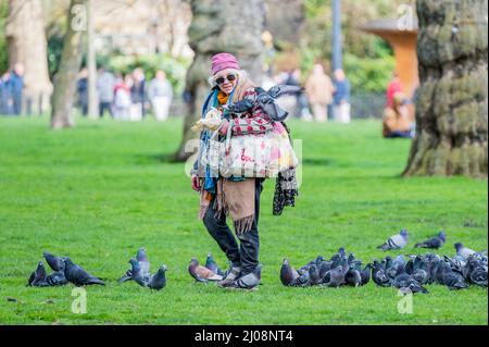 Londra, Regno Unito. 17th Mar 2022. Una donna che alimenta i piccioni in Green Park al sole di primavera. Credit: Guy Bell/Alamy Live News Foto Stock