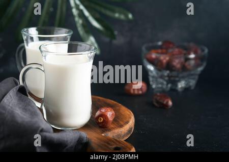 Ramadan Kareem cibo e bevande. Piatto di datteri, bicchiere di latte e ramo di palma di datteri su sfondo nero. Stile di vita musulmano giusto. Cibo vegetariano. S Foto Stock