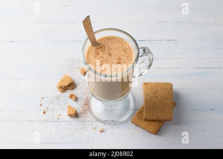 Tè piccante con latte in una tazza di vetro e biscotti di pan di zenzero su sfondo grigio chiaro blu Foto Stock