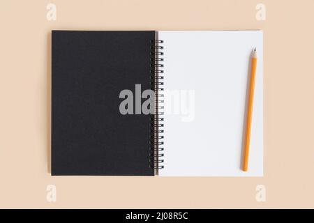 Taccuino con matita. Aprire il notebook su sfondo beige, il blocco note a spirale per ufficio sul tavolo con pagine vuote. Vista dall'alto. Pagina bianca per la scrittura. Foto Stock