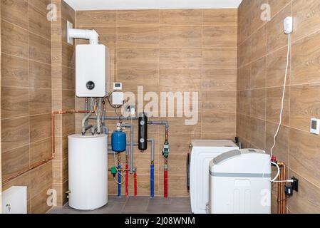 Un moderno locale caldaia a gas rivestito di piastrelle in ceramica che imitano legno, attrezzatura completa visibile sala caldaia con lavatrice e addolcitore d'acqua. Foto Stock