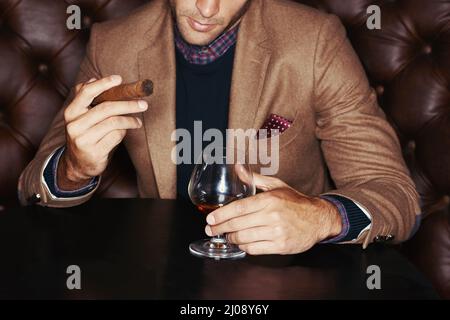 Mostrando la sua ricchezza. Un uomo alla moda che beve whiskey e fuma un sigaro. Foto Stock