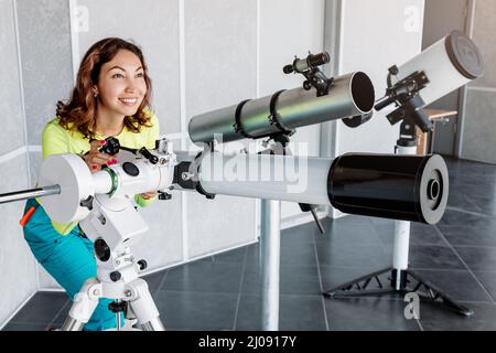 Donna felice in un osservatorio spaziale guarda un meteorite o il sole attraverso un telescopio ottico professionale. Concetto di occupazione e studio astronomico Foto Stock