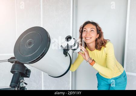 Donna felice in un osservatorio spaziale guarda un meteorite o il sole attraverso un telescopio ottico professionale. Concetto di occupazione e studio astronomico Foto Stock