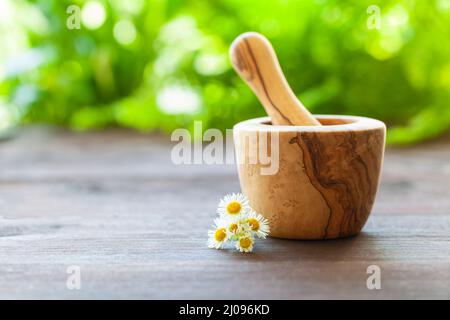 Concetto omeopatico. Un mortaio di legno e pestello con calendula su un tavolo di legno. Sfondo verde sfocato. Foto Stock