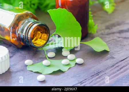 Una bottiglia medica marrone, pillole e foglie di ginkgo decorate su sfondo di legno. Concetto omeopatico. Foto Stock