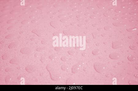 Primo piano di goccioline d'acqua sul piano in acrilico dopo la pioggia in rosa pastello Foto Stock