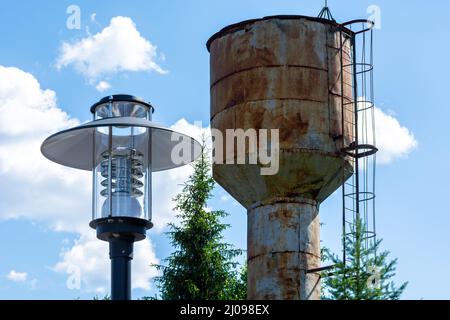 Lampada di strada e una vecchia torre d'acqua arrugginita contro un cielo blu. Foto Stock