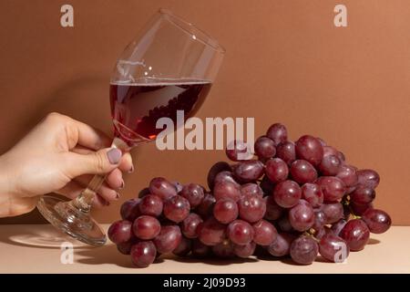 La donna tenera le dita tiene un bicchiere di vino rosso fragrante sullo sfondo dell'uva. Concetto di bevande alcoliche. Dessert. Foto Stock