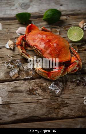 Vista dall'alto di gustoso granchio cotto con cubetti di ghiaccio e lime su sfondo rustico in legno. Pasto delizioso. Concetto di pesce. Foto Stock