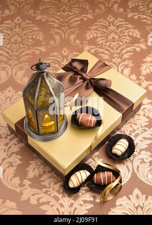 Lampada tradizionale Ramadan posta su scatola regalo dorata con cioccolatini daccatati. Sfondo islamico festivo. Foto Stock