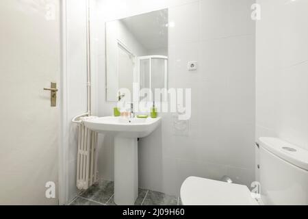 Bagno con piedistallo abbinato lavello in porcellana bianca, specchio quadrato senza cornice e radiatore in ghisa Foto Stock