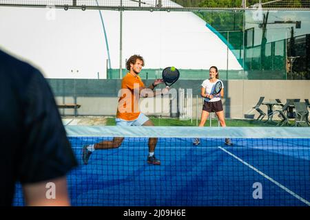 L'istruttore insegna ai giovani come giocare a padel sul campo da tennis all'aperto - misto padel match outdoorin un campo di padel in erba blu - Sport e amici conc Foto Stock