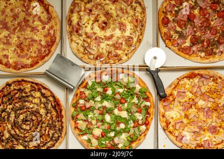 Deliziose pizze assortite appena sfornate insieme a taglierini per pizza in scatole per la consegna a domicilio Foto Stock