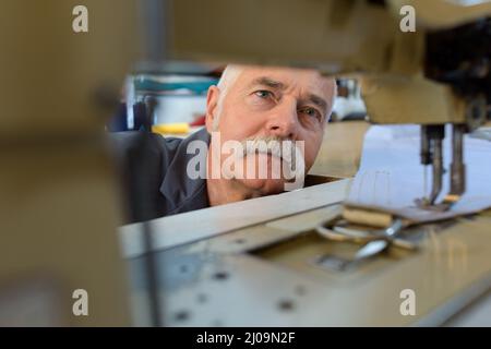 Meccanico senior di riparazione di macchina per cucire industriale in fabbrica Foto Stock