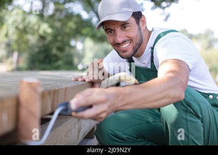 carpentiere bell'uomo giovane che installa un pavimento di legno all'aperto Foto Stock