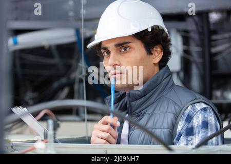 giovane costruttore che guarda l'installazione elettrica nel soffitto dell'edificio Foto Stock