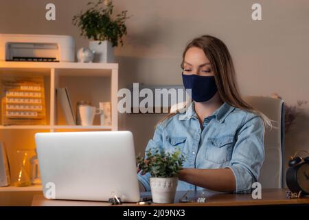 Giovane donna in maschera protettiva viso spaventato nastri laptop sullo sfondo dell'ufficio. Concetto di pandemia di coronavirus nel mondo e cura della salute. Foto Stock