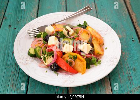 Insalata greca con verdure fresche e formaggio feta in grande piatto bianco su tavola turchese con due forchette orizzontali Foto Stock