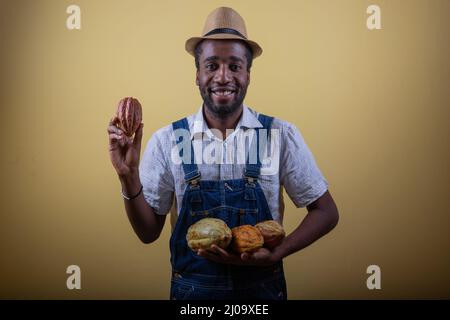 Un agricoltore africano tiene in mano i fagioli di cacao, è felice per il buon raccolto Foto Stock